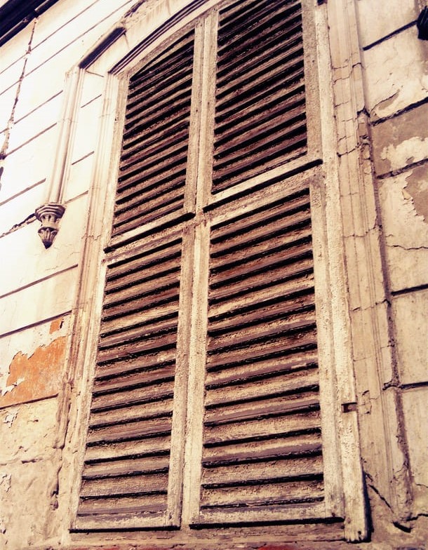 Geschlossene Fensterläden an einem hohen Fenster mit Verkleidungsbrettern.